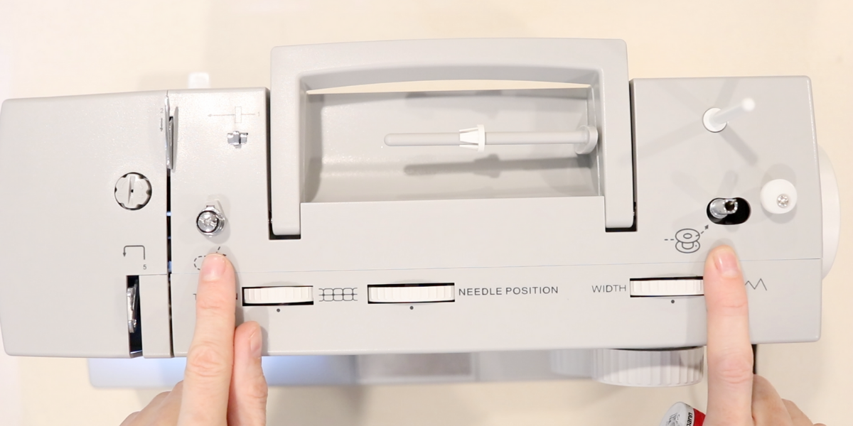 two fingers are pointing to bobbin winding points on the top of a gray singer sewing machine.