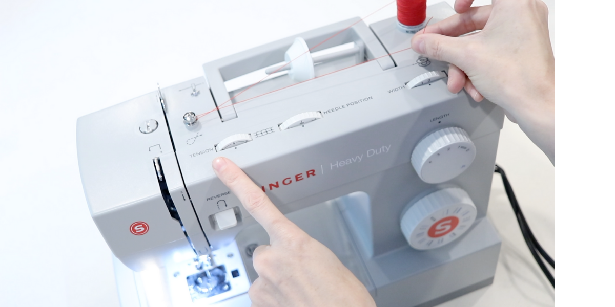 right hand holding the red thread while preparing to thread a sewing machine