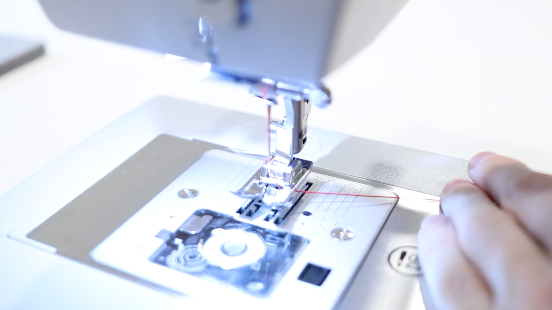 Close up of a sewing machine foot that has been threaded with red thread.